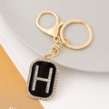 Close-up of golden letter H keychain with sparkling rhinestones on black enamel finish - Letter H