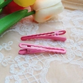 Macro view of pink wavy metal hair clips on white lace fabric with tulip background - Pink
