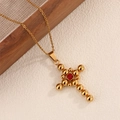 Detail of gold cross necklace featuring polished spheres and a central red zircon stone - Red Zirconia