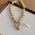 Gros plan d'un collier cœur en acrylique marbré avec perles dorées sur tissu texturé - Collier / Blanc