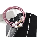 Vista macro di elastici per capelli tre in uno con perle finte e perline d'oro su marmo - Rosa antico
