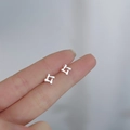 Macro view of geometric silver cross earrings held on a fingertip for size comparison - Geometric Four-corner / Silver
