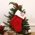 Red knit Christmas stocking with white cuff featuring red embroidered letter M and holly - Letter M