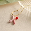 Détail du pendentif lettre K en émail rose et rouge sur une fine chaîne dorée - Style-X