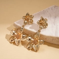 Close-up of golden metallic flower earrings on marble surface with soft natural lighting - Gold