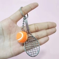 Mini tennis racket and orange ball keychain for bags shown in high detail on pink background - 2cm Ball / Orange