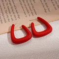 Macro view of matte red acrylic C-shaped earrings on a vintage newspaper background - Red Round