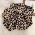 Nahaufnahme eines Haargummis mit Leopardenmuster aus Textilstoff auf Leinenhintergrund - Hell-Leopard-Haargummi