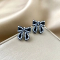 Close-up of elegant black bow stud earrings with small white pearls on satin - Black Bowknot Pearl Style (E1316-1)