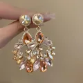 Handheld view of ornate geometric drop earrings with multi-color stones and small tassels - Gold Water Drop