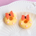 Macro view of a yellow resin donut with a red bow and pink dots on a white plate - Large Bow - Yellow Base + Orange