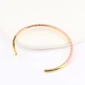 Detail of gold open bangle with pink enamel stripes on a white display stand - Pink
