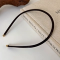 Detalle de la diadema de cuero oscuro con puntas de metal dorado sobre un libro - Café Oscuro