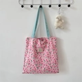Detail of floral tote bag with light blue handles and a decorative woven brand label - Lusi Portrait