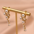 Elegant gold drop earrings featuring tiered white pearls on a stylish golden display stand - Shell Pearl Style