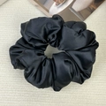 Detail of a large black satin scrunchie with soft pleated texture on a beige fabric background - Black