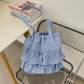 Detailed close-up of blue and white gingham tote bag with layered ruffle trim on a chair - Blue