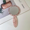 Macro shot of pink marble pattern acetate hand mirror on a minimalist white desk - Pink