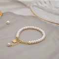 Elegante bracciale di perle d'acqua dolce con ciondolo portafortuna d'oro su fondo grigio - Bracciale di Perle Tonde da 5MM