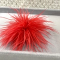 Macro detail of vibrant red ostrich feather brooch on a grey velvet display tray - Red