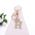Golden keychain with rhinestone-encrusted letter H and crown charm on white stand - Letter H / Gold
