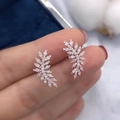 Elegant rose gold wheat leaf earrings with zircon inlay held by hand on blue background - Rose Gold