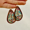 Close-up of teardrop earrings featuring stained glass church patterns and wooden frames - Stained Glass Style