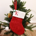 Red knitted Christmas stocking with white cuff and embroidered letter K hanging on tree - Letter K