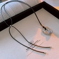 Detalle de un colgante metálico de forma orgánica en un collar de cordón negro fino - Plateado