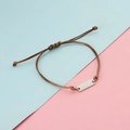 Close-up of brown braided cord bracelet with polished silver metal bar on a dual-tone background - Steel Color Brown Rope