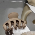 Detailed close-up of a khaki glossy hair claw clip with its reflection on a mirror surface - Milk Tea