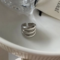 Nahaufnahme eines silbernen, dreilagigen, wellenförmigen offenen Rings in einer Schale - Dreischichtige Offene Ring / Silber