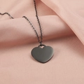 Collar con colgante de corazón negro mate sobre un fondo de tela rosa con textura - Negro