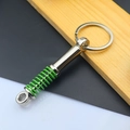 Close-up of a silver metal shock absorber keychain with a vibrant green spring - Shock Absorber / Green