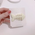 Cute cream white fishbone hair clip held in hand against a white paper card - Beige