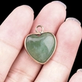 Green jade heart pendant in golden frame held by fingers over black background - Green Aventurine Gold Edging