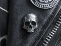 Close-up of vintage silver skull badge pinned on black leather jacket with gothic details - Single Skull Head