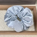 Close-up of a light blue silk scrunchie on a wooden tray with a glass base - Blue