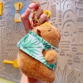 Plush capybara keychain wearing a tropical palm leaf shirt with a golden lobster clasp - Vacation Capybara Green Shirt