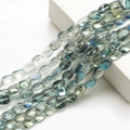 Macro shot of 10x12mm teal crystal beads with rainbow luster on white display block - Semi-transparent Green