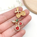 Golden cherry pendant with red heart crystals and green enamel leaf held by fingers - KC Gold Red Rhinestone Heart Fruit Cherry (23421)
