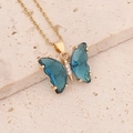 Detail of a gold butterfly necklace with blue wings and zircon inlay on a stone surface - Dark Blue