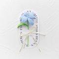 Close-up of handmade blue crochet lily with green leaves and Love Is Eternal ribbon - Blooming Tulip - Light Blue