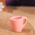Miniatur-Tasse aus rosa Harz für Puppenhaus-Deko auf hellem Holzgrund - Mini-Becher / Rosa