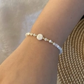 Detail of beaded shell bracelet with golden letter V charm on a textured background - Letter V Style (V)