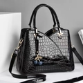 Detail of black crocodile texture bag with glossy finish and cherry bag charm accessory - Black