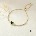 Macro detail of gold adjustable heart bracelet featuring a green gem and pave crystals - Green
