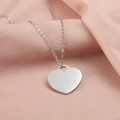 Detalle de collar con colgante de corazón plateado sobre fondo de tela rosa suave - Color Acero