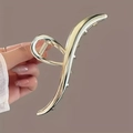 Large wave-shaped gold metal hair claw clip held by hand for a minimalist hair style - Gold