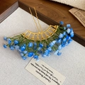 Dettaglio della forcina dorata ondulata con eleganti fiori piccoli blu e bianchi - Blu